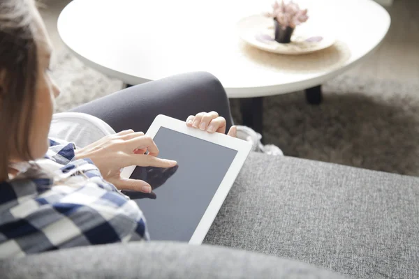 Mujer joven sentada en un sofá en la sala de estar y usando una tableta digital —  Fotos de Stock