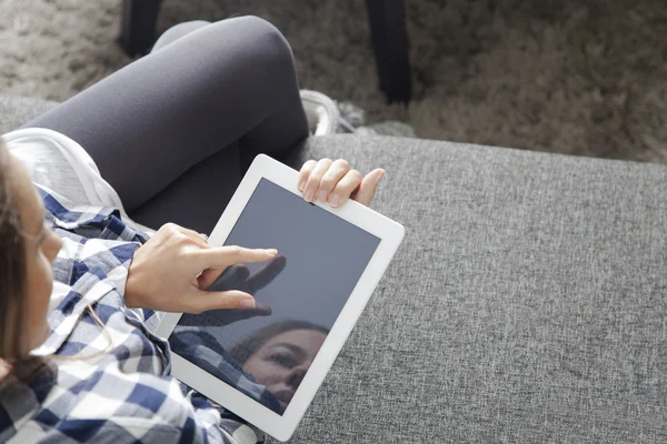 Oturma odasında kanepede oturan ve dijital tablet kullanarak genç kadın