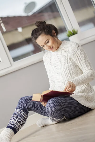 Ung kvinna läser en bok hemma — Stockfoto