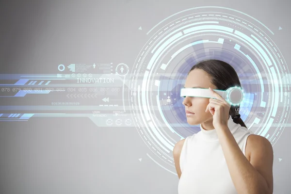 Mujer joven con gafas inteligentes futuristas sobre fondo gris —  Fotos de Stock