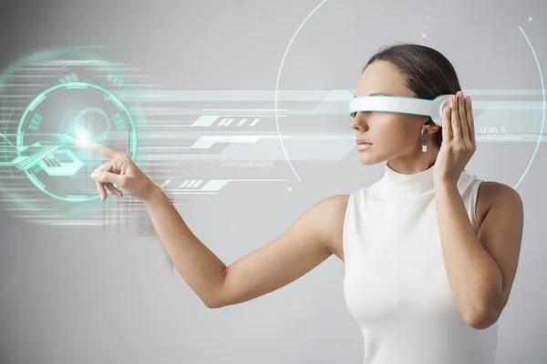 Mujer joven con gafas inteligentes futuristas sobre fondo gris —  Fotos de Stock