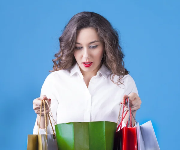 Surprised girl with shopping bags on blue background. — Stock Photo, Image