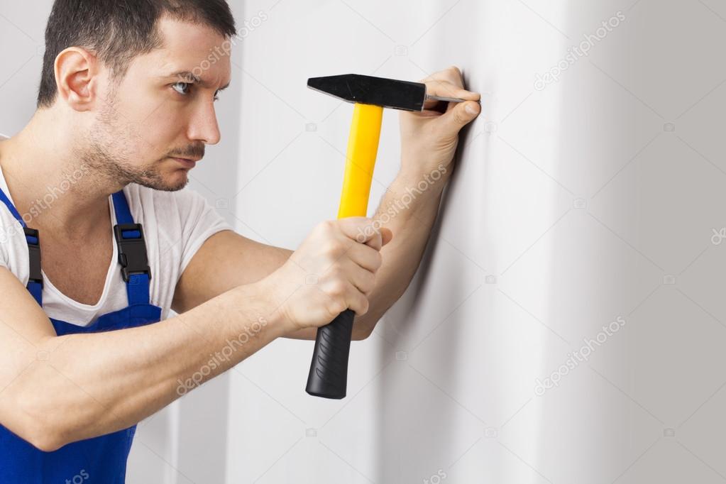 вбить молотком в стену. прибить молотком. гвоздь в стене. молоток забивает гвоздь. мужчина забивает гвоздь.