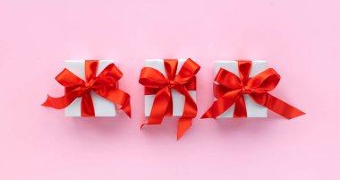 Noel kompozisyonu. Pastel pembe arka planda kırmızı kurdeleli üç hediye kutusu. Düz yatış, üst görünüm