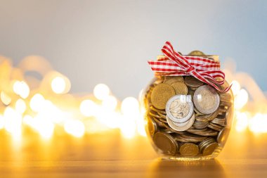 Noel ışıklarının önünde bozuk para dolu tasarruf kavanozu. Tatil masrafları için birikmiş paralar.