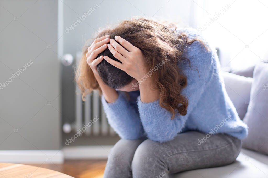 Young depressed woman sitting on sofa in living room. She feeling sad and worried suffering depression in mental health. Problems and broken heart concept.