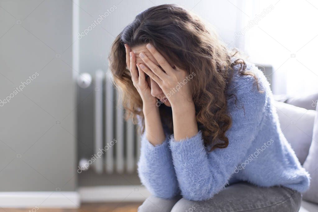 Young depressed woman sitting on sofa in living room. She feeling sad and worried suffering depression in mental health. Problems and broken heart concept.