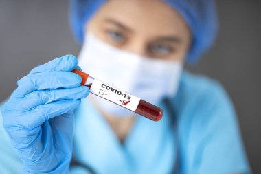 Solunum maskesi takan hemşire COVID-19 için pozitif kan testi sonuçlarını tutuyor.