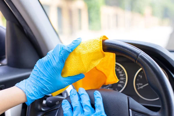 Female hands with blue gloves wiping car steering wheel with disinfectant wipe.