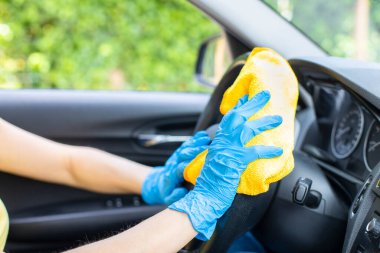 Mavi eldivenli kadın elleri dezenfektanla direksiyon simidini siliyor..