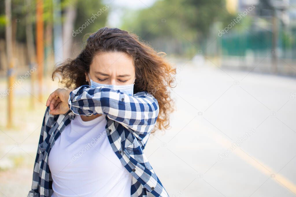 Woman with face mask sneezing into elbow while walking in the street