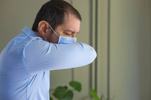 Young man with face mask sneezing into elbow