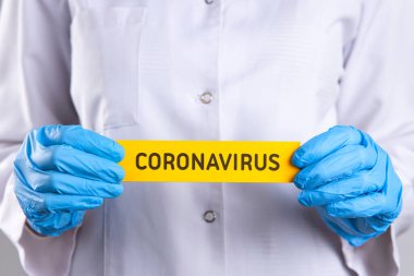 Üniformalı kadın doktor elinde koronavirüs yazan sarı bir levha tutuyor. 