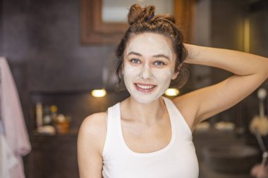 Evde yüz maskesi takan genç bir kadın.