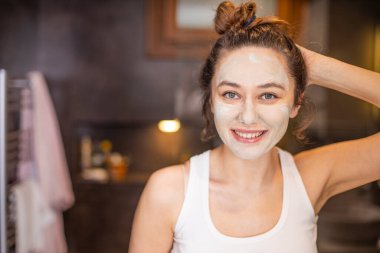 Evde yüz maskesi takan genç bir kadın.