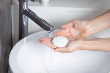 Genç bir kadın ellerini sabunla yıkıyor.