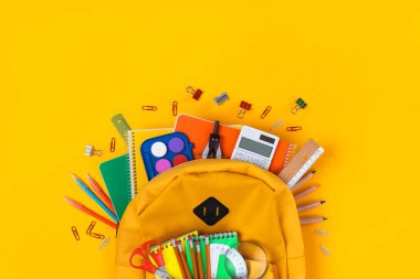 Okul malzemeleriyle dolu sırt çantası sarı alana yayılıyor. Okul konseptine dönüş.
