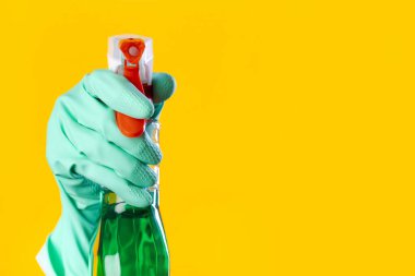 Eldivenli kadın, sarı arka planda pencere spreyi tutuyor.