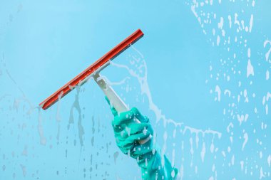 Bulaşık eldivenleri ve silecekler mavi sabunlu camda izole edilmiş. Cam sileceği sabun köpüğüyle bardağı sil.