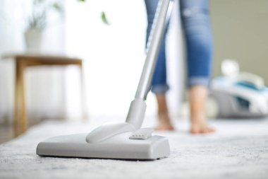 Genç ev hanımı elektrikli süpürgeyle evi temizliyor. Oturma odasının zeminini temizlemek için elektrikli süpürge kullanmak.