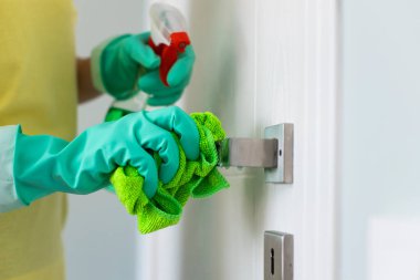 Kadın dezenfekte spreyiyle kapı kolunu temizliyor.