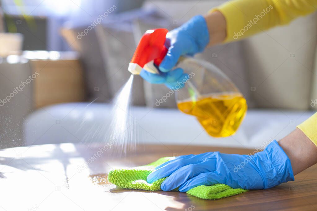 Woman with gloves cleaning with spray detergent and rag on work surface 