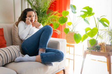 Genç bir kadın evde telefonla konuşuyor, endişeli bir kadın elinde akıllı bir telefon tutuyor ve oturma odasında arama yapıyor.