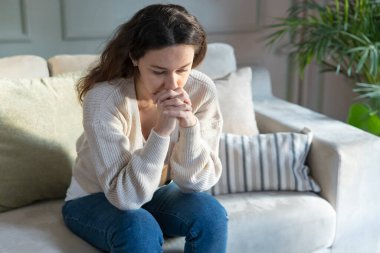 Oturma odasındaki kanepede oturan bunalımlı genç kadın. Ruh sağlığında depresyon geçirdiği için üzgün ve endişeli. Sorunlar ve kırık kalp kavramı.