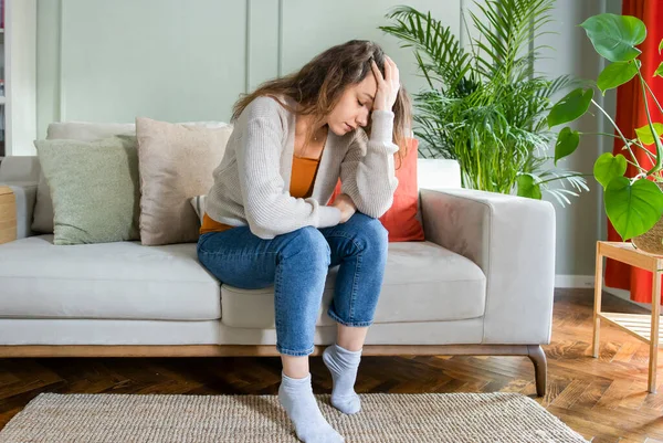 リビングルームでソファに座っている若い落ち込んでいる女性 彼女は心の健康の中で悲しいと悩みのうつ病を感じます 問題と壊れた心の概念 — ストック写真