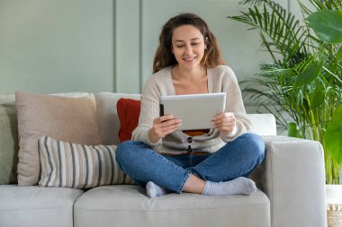 Kanepede oturan ve tablet kullanan genç bir kadın. İnternetten film izliyorum..