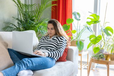 Evdeki kanepede dizüstü bilgisayar kullanan bir kadın. Rahat bir çalışma ortamı, serbest çalışan