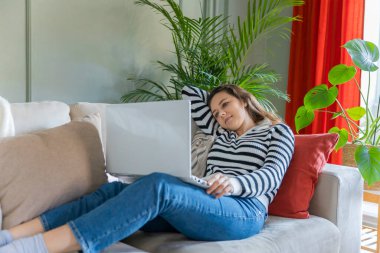 Evdeki kanepede dizüstü bilgisayar kullanan bir kadın. Rahat bir çalışma ortamı, serbest çalışan