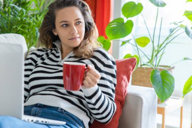 Evdeki kanepede dizüstü bilgisayar kullanan bir kadın. Rahat bir çalışma ortamı, serbest çalışan