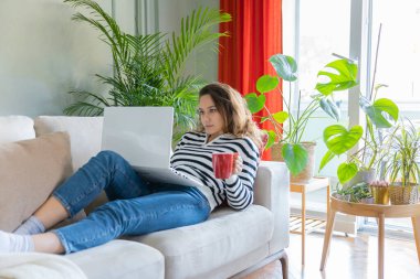 Evdeki kanepede dizüstü bilgisayar kullanan bir kadın. Rahat bir çalışma ortamı, serbest çalışan