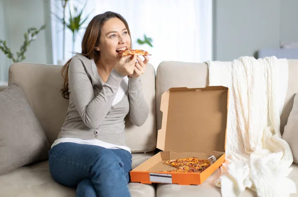 Young woman eating a slice of pizza at home. Attractive young woman eating tasty pizza in living room.