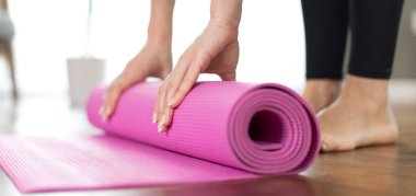 Genç kadın egzersiz yaptıktan ve evde meditasyon yaptıktan sonra yoga minderini yuvarlıyor.