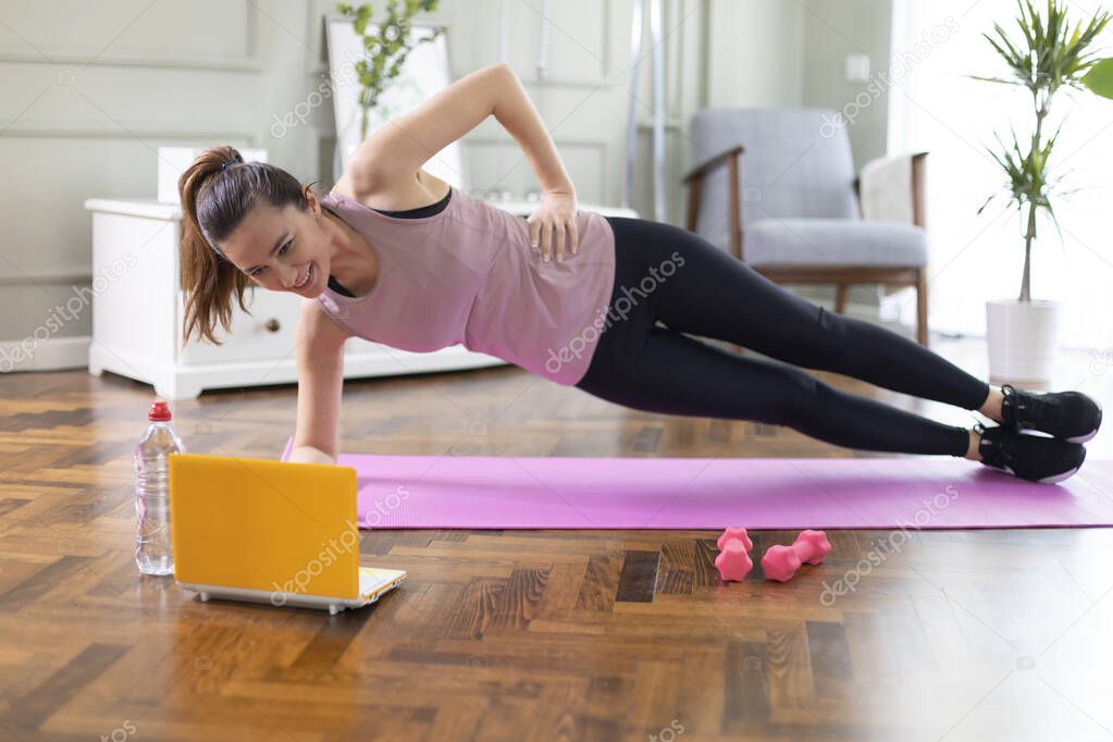 Young woman exercising at home in a living room. Video lesson. She is repeating exercises while watching online workout session