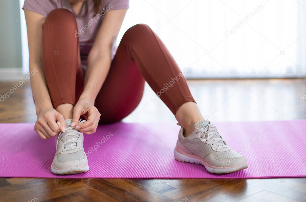 Sporty young woman tying the shoe laces on exercise mat in living room