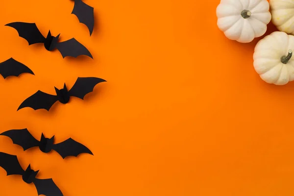 Happy halloween holiday concept. Halloween decorations, pumpkins and bats on orange background. Halloween party greeting card mockup with copy space. Flat lay, top view, overhead.