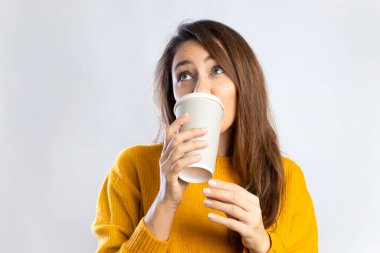 Gülümseyen genç kadın beyaz arka planda kağıt bardaktan kahve içiyor.