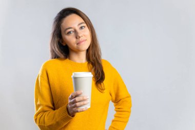 Gülümseyen genç kadın beyaz arka planda kağıt bardaktan kahve içiyor.