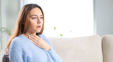 Genç bir kadın ağrılı boynuna dokunuyor. Grip, soğuk algınlığı ve enfeksiyon yüzünden boğazı ağrıyor.