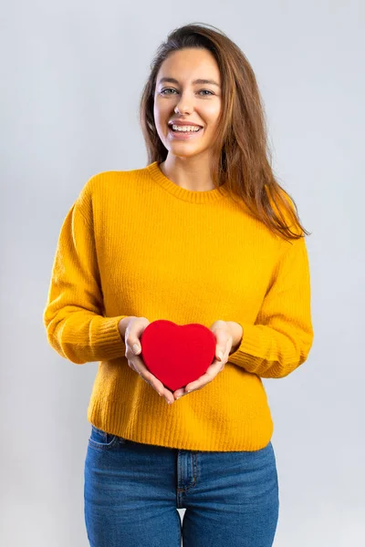 幸せな若い女性は灰色の背景に隔離された赤いハート型の箱を保持する バレンタインの贈り物 — ストック写真