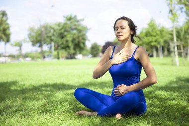 Parkta meditasyon yapıyor yeşil çimenlerin üzerinde oturan genç kadın