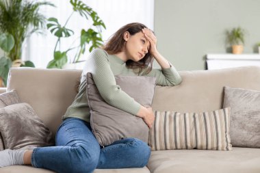 Oturma odasındaki kanepede oturan bunalımlı genç kadın. Ruh sağlığında depresyon geçirdiği için üzgün ve endişeli. Sorunlar ve kırık kalp kavramı.