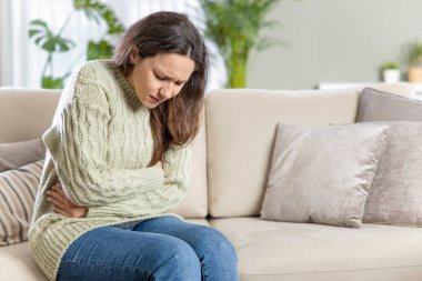 Evdeki kanepede oturan genç bir kadın midesinde bir ağrı var.