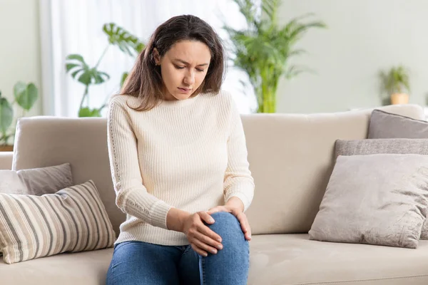 Mujer Joven Con Dolor Rodilla Sentada Sofá Apartmen — Foto de Stock