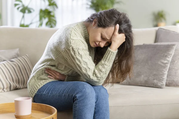 若い女性は胃の痛みで家にソファに座っている 胃の痛み うつ病の概念 — ストック写真