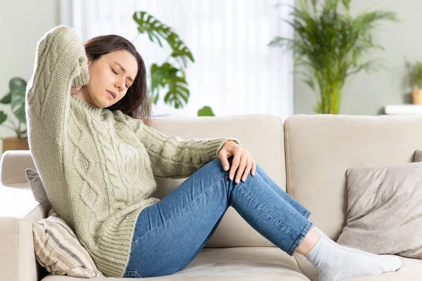 Jonge Vrouw Zit Thuis Haar Bank Raakt Achterkant Van Haar — Stockfoto