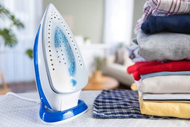 Ütü masasının üzerinde duran ütü ve katlanmış temiz giysiler.